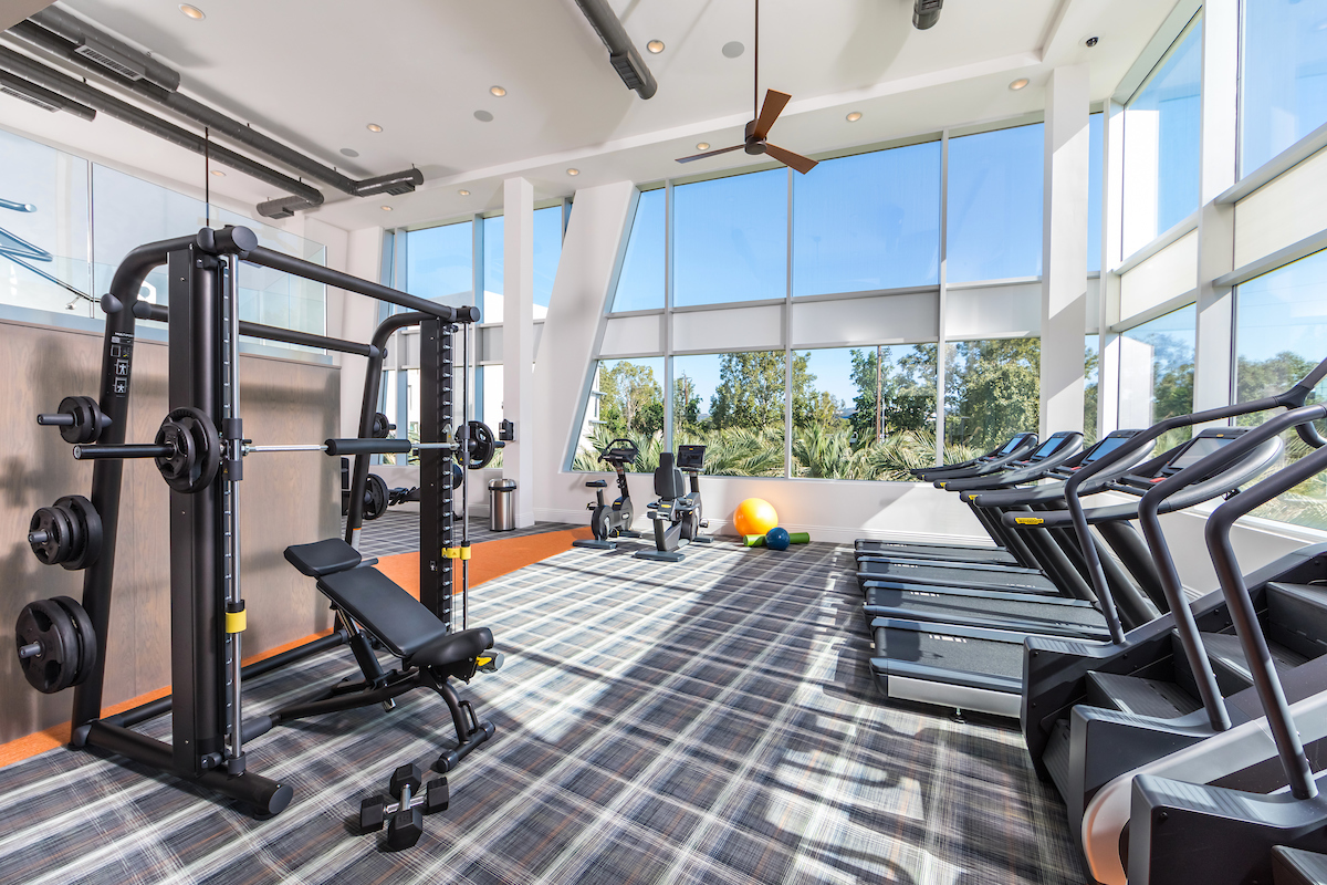 A bright fitness center with large windows at the Aliso Apartments.