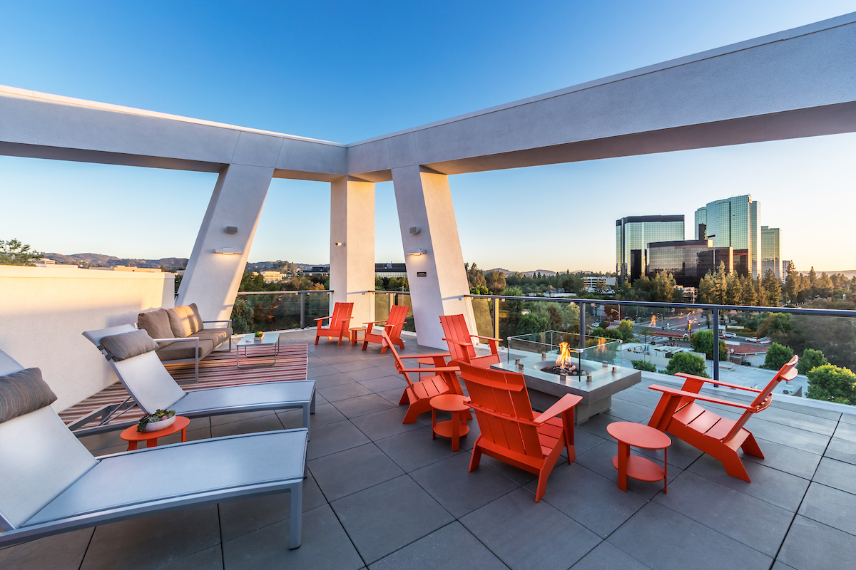 Lounge seating and a fire pit on a rooftop terrace overlooking the cityscape.