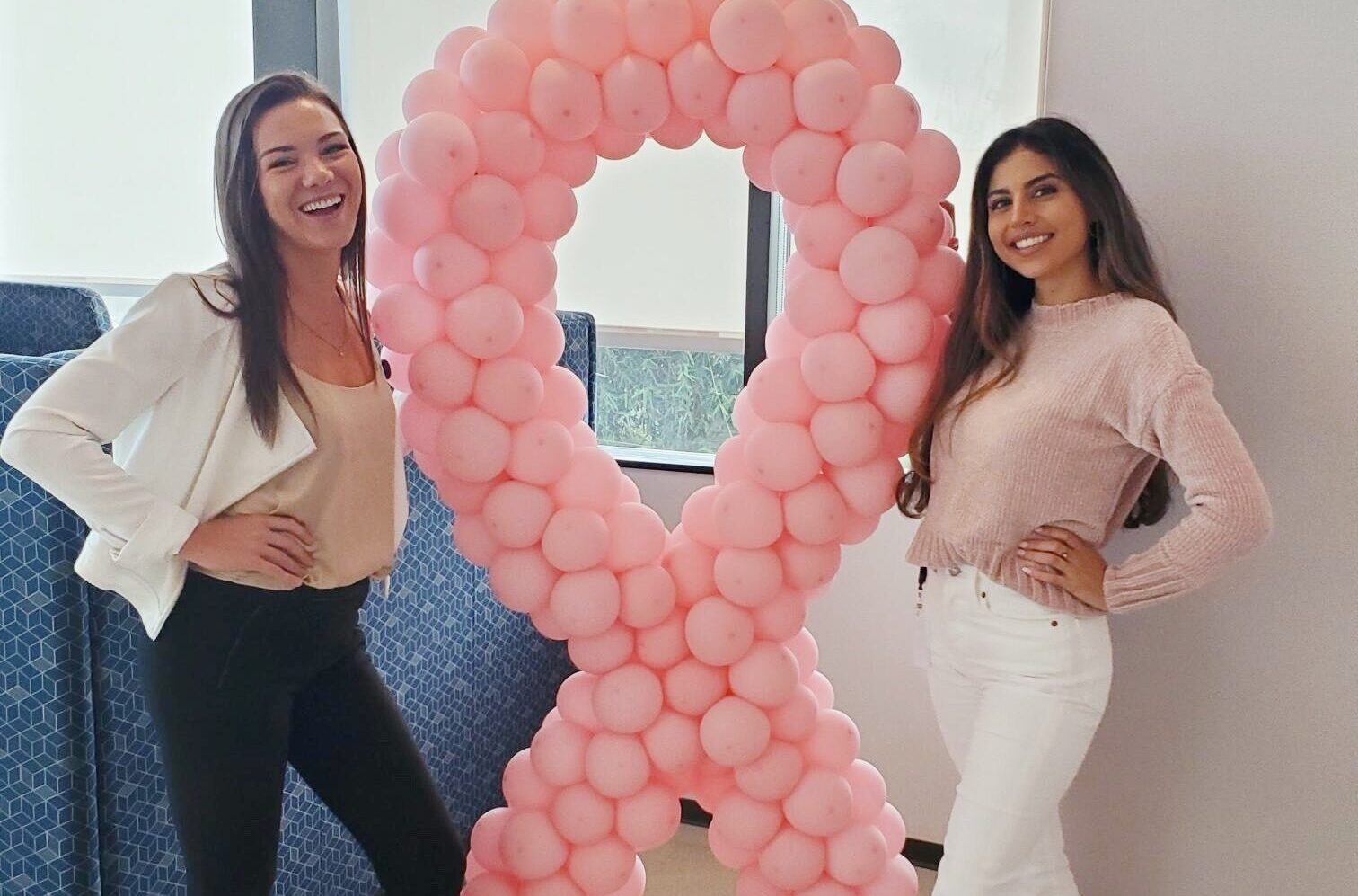 Two Fairfield associates stand next to a breast cancer ribbon balloon arch.