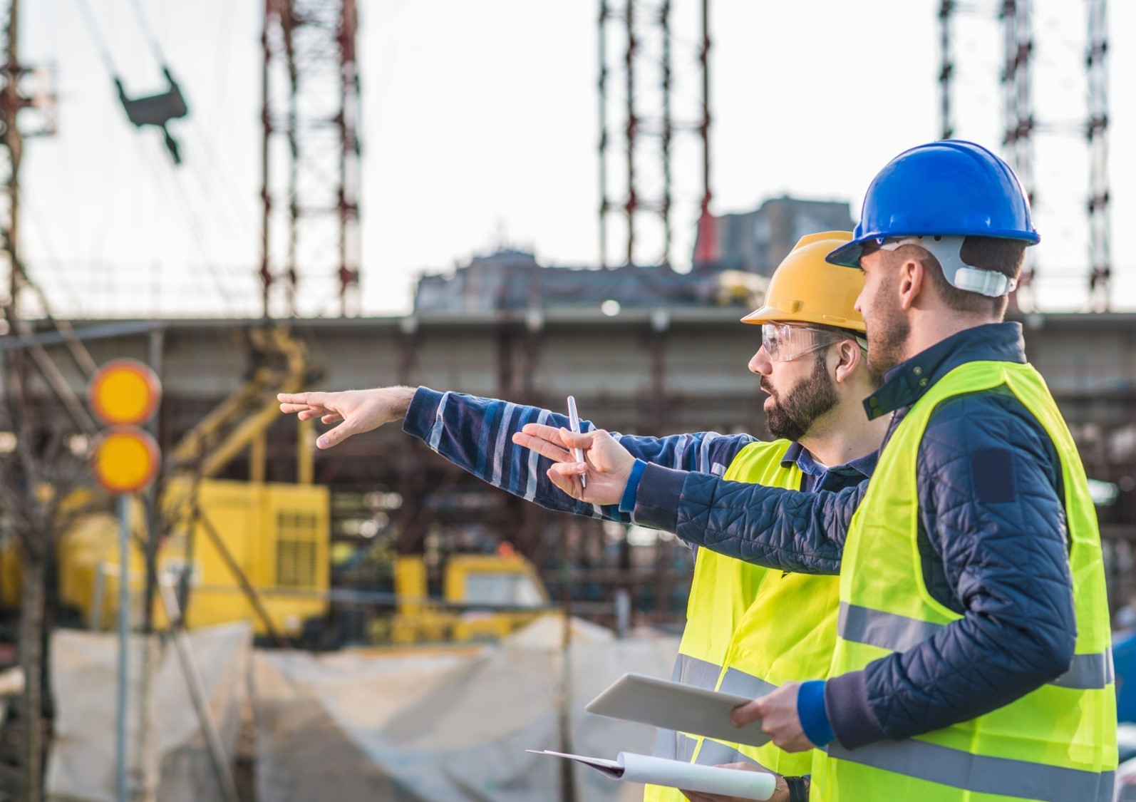 Two construction workers discuss a construction site.