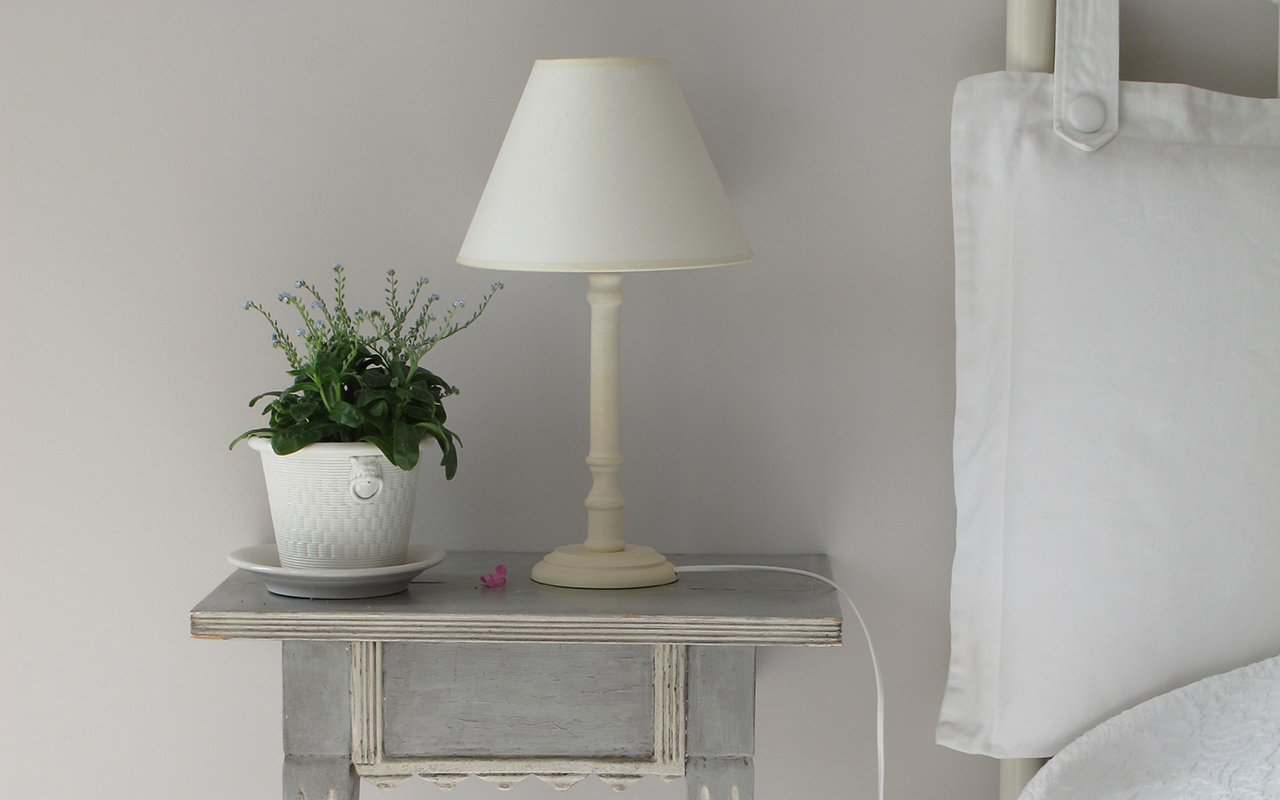 A close-up of a lamp and plant on a beside nightstand.