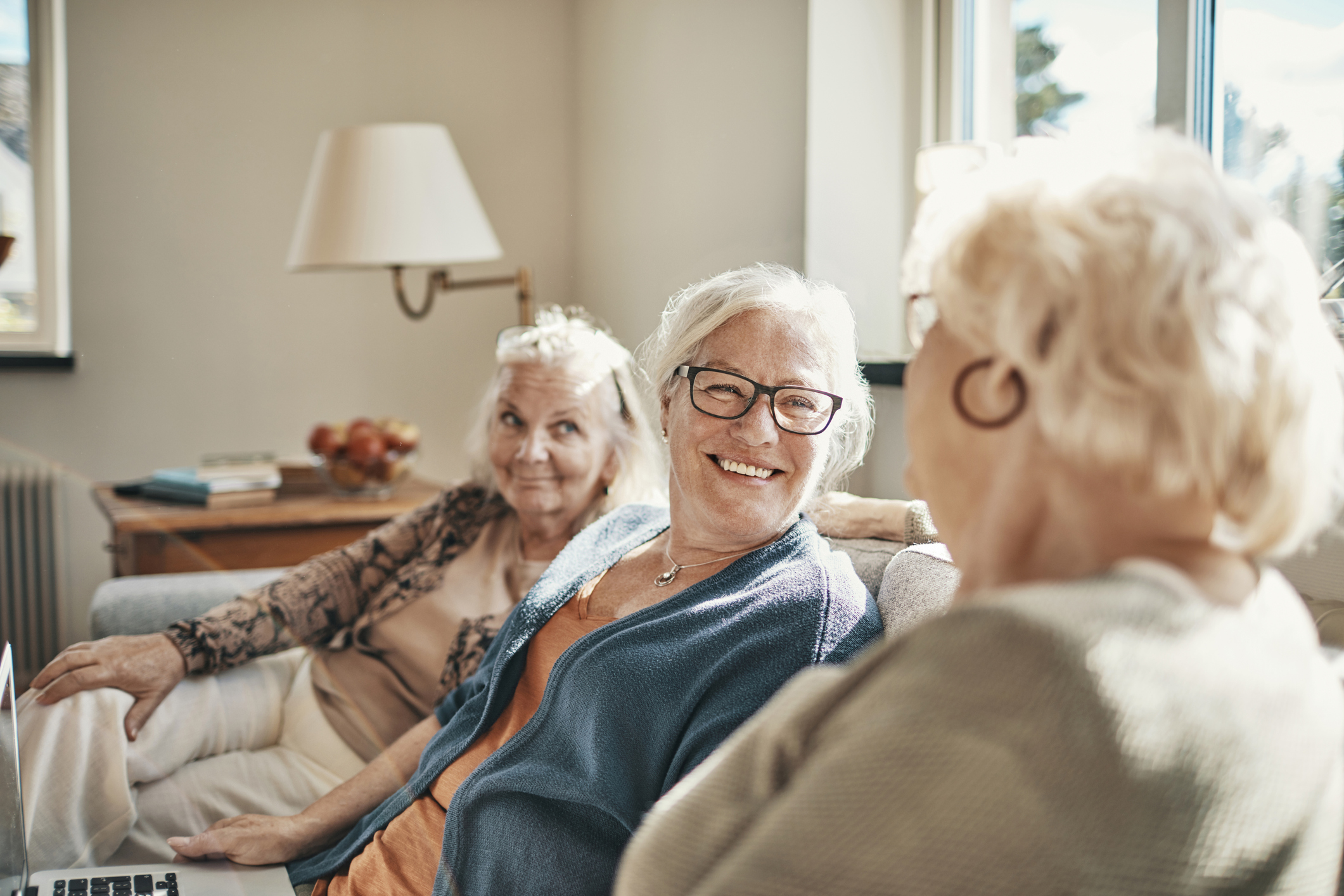 3 senior women sit on the couch  and laugh together.