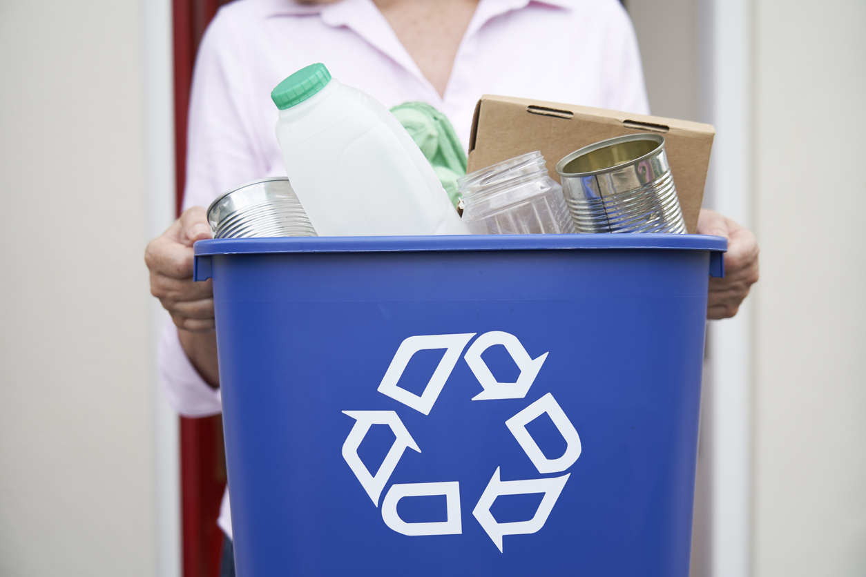 A close-up of a woman carrying a full recycle bin.