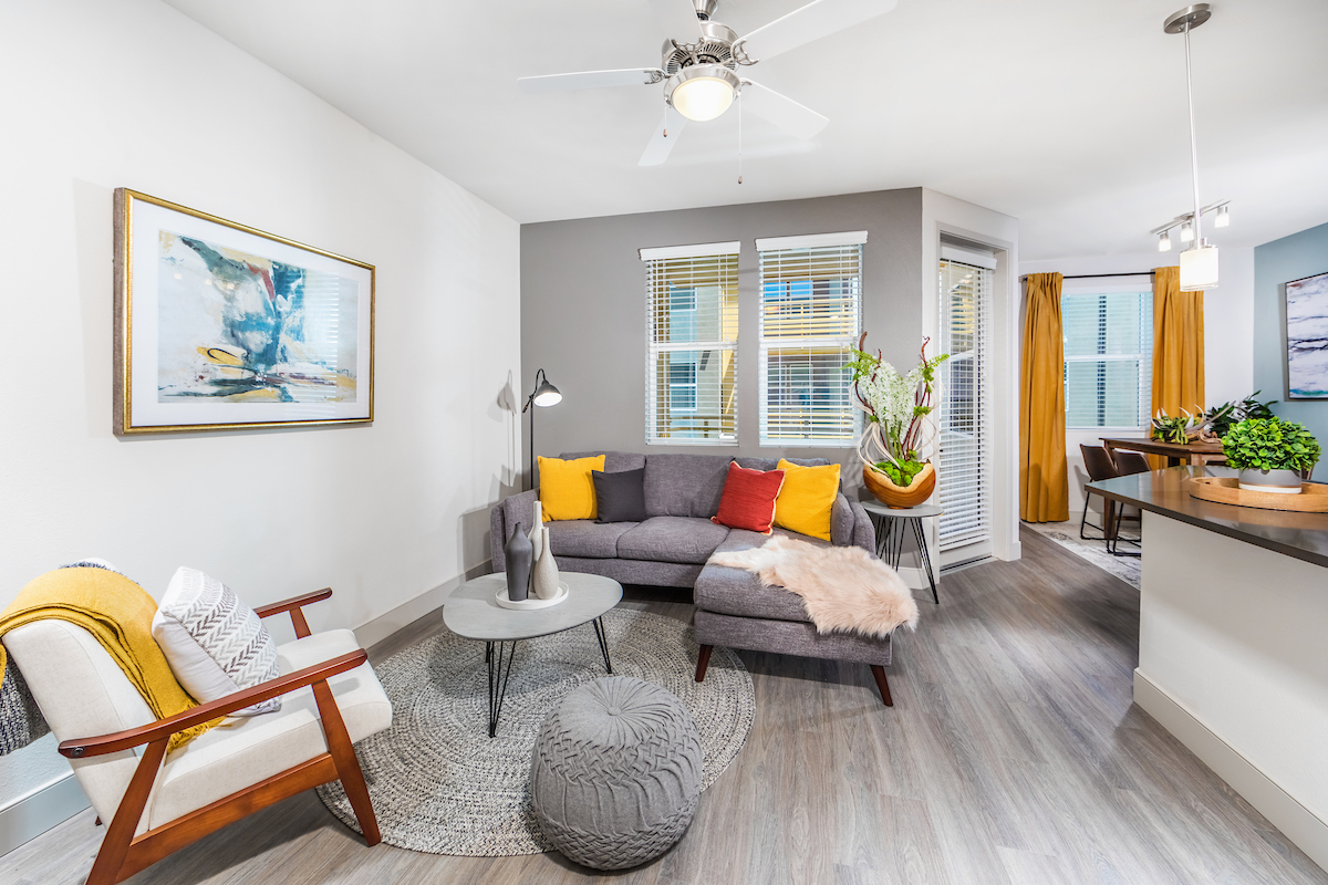 A modern, brightly-decorated apartment living room leading into the dining room and a patio.