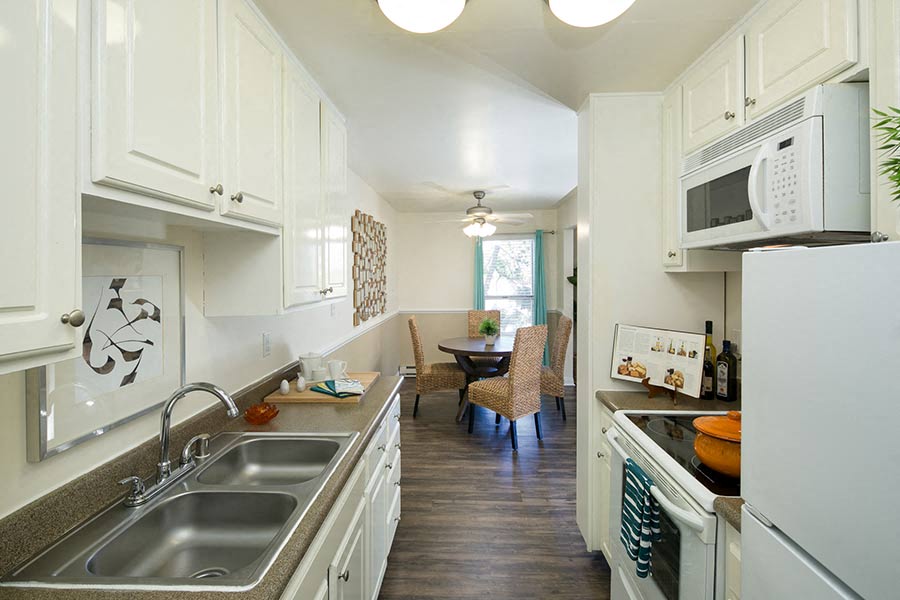 A kitchen with a double sink leading to the dining room at the Bayside Apartments in Pinole, California.