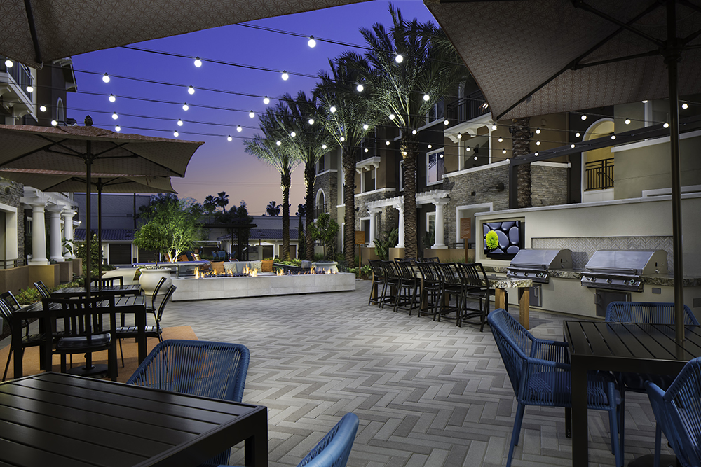 Evening at Valentia Apartments' outdoor courtyard with string lights and barbecue grills