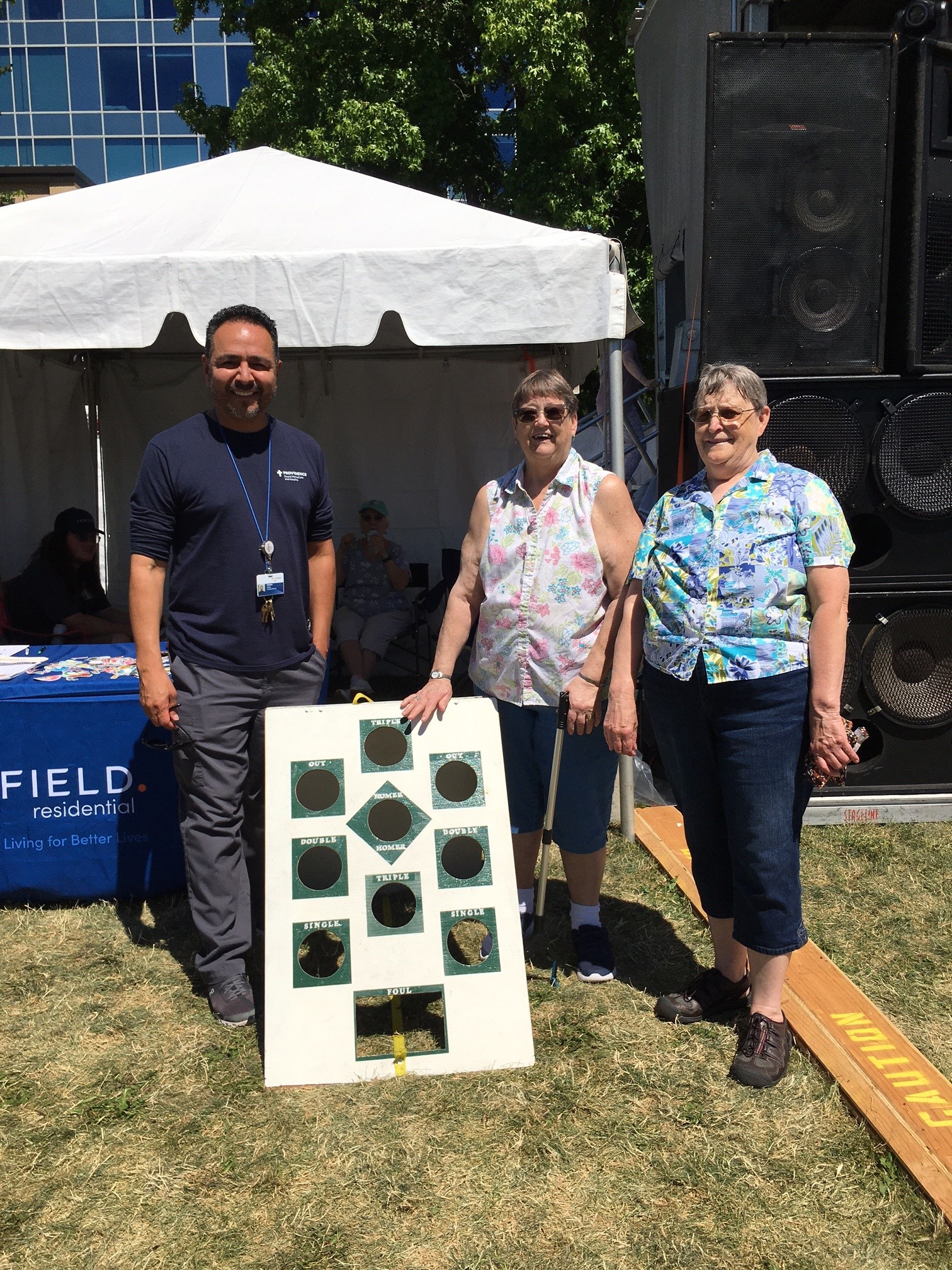 Boardwalk’s 2 Pattys (Patty Hurst and Patty Hicks) show Lakefair 50+ guest Carlos Alaniz from Providence SoundHomeCare and Hospice how to play Bean Bag Baseball.