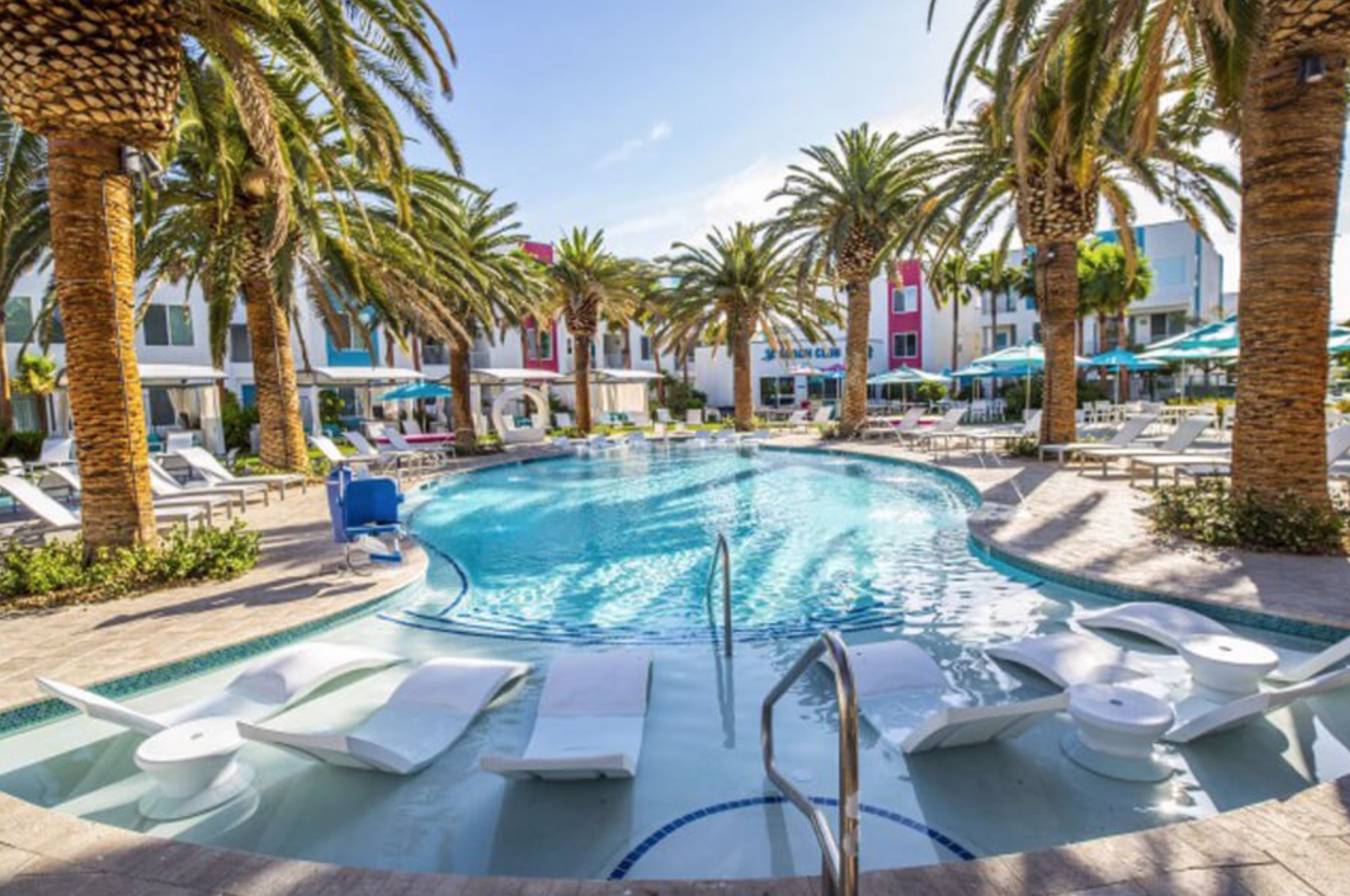 A luxury, palm tree lined pool with lounge seating.